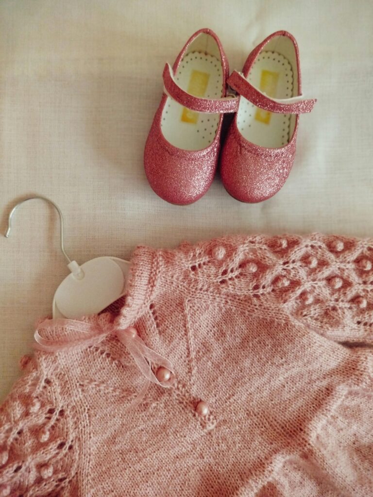 Charming pink baby dress and glitter shoes set on a soft background.